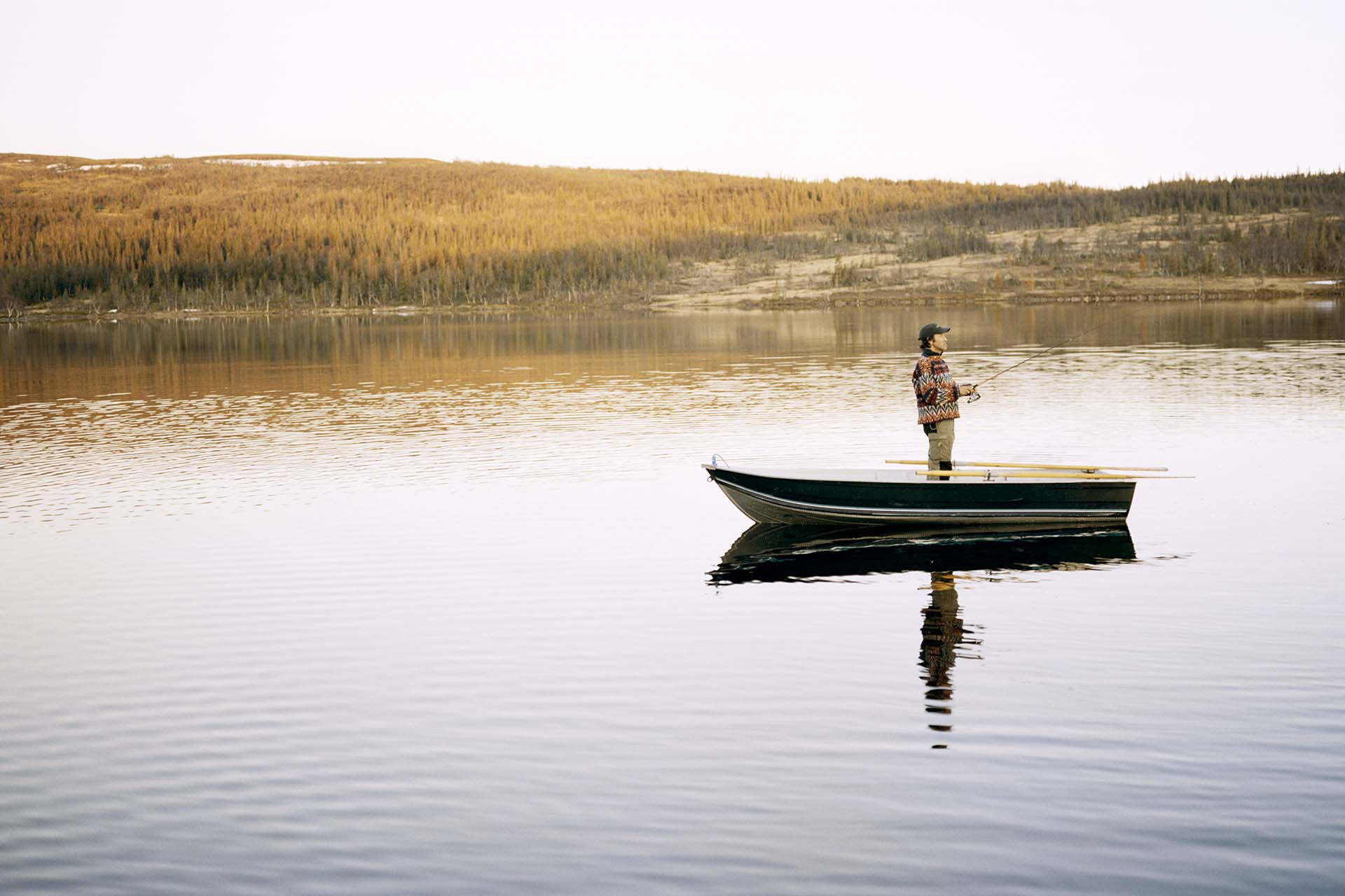 En ung man fiskar på en liten eka längs en sjö