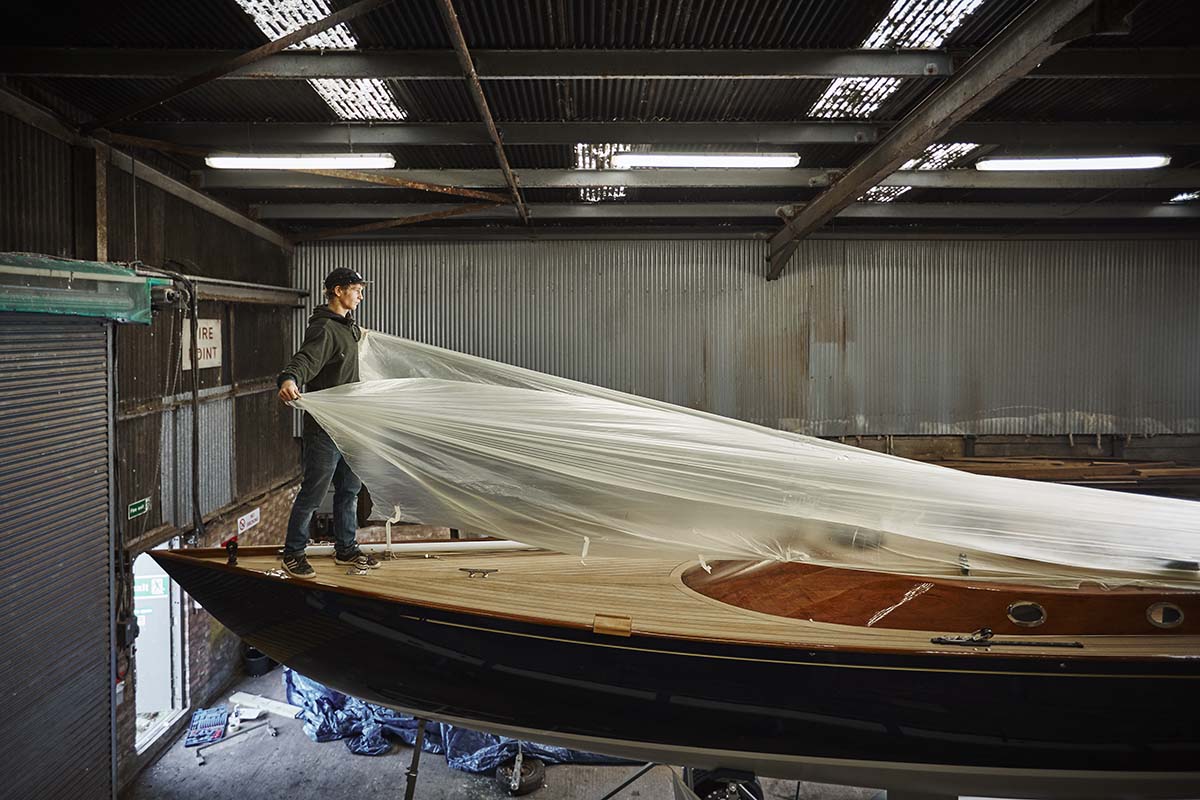En ung man täcker för en båt inne i ett garage